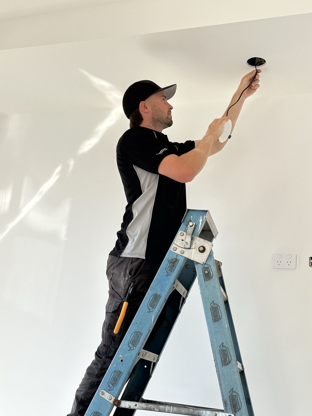Electrician on a ladder fitting an LED downlight into a new ceiling