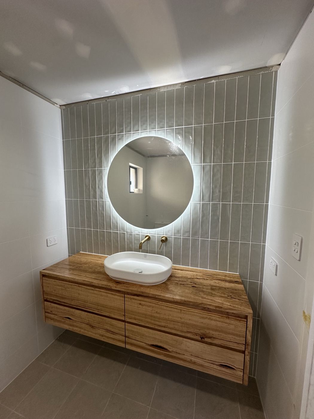Round backlit LED mirror above a timber vanity with brass tapware